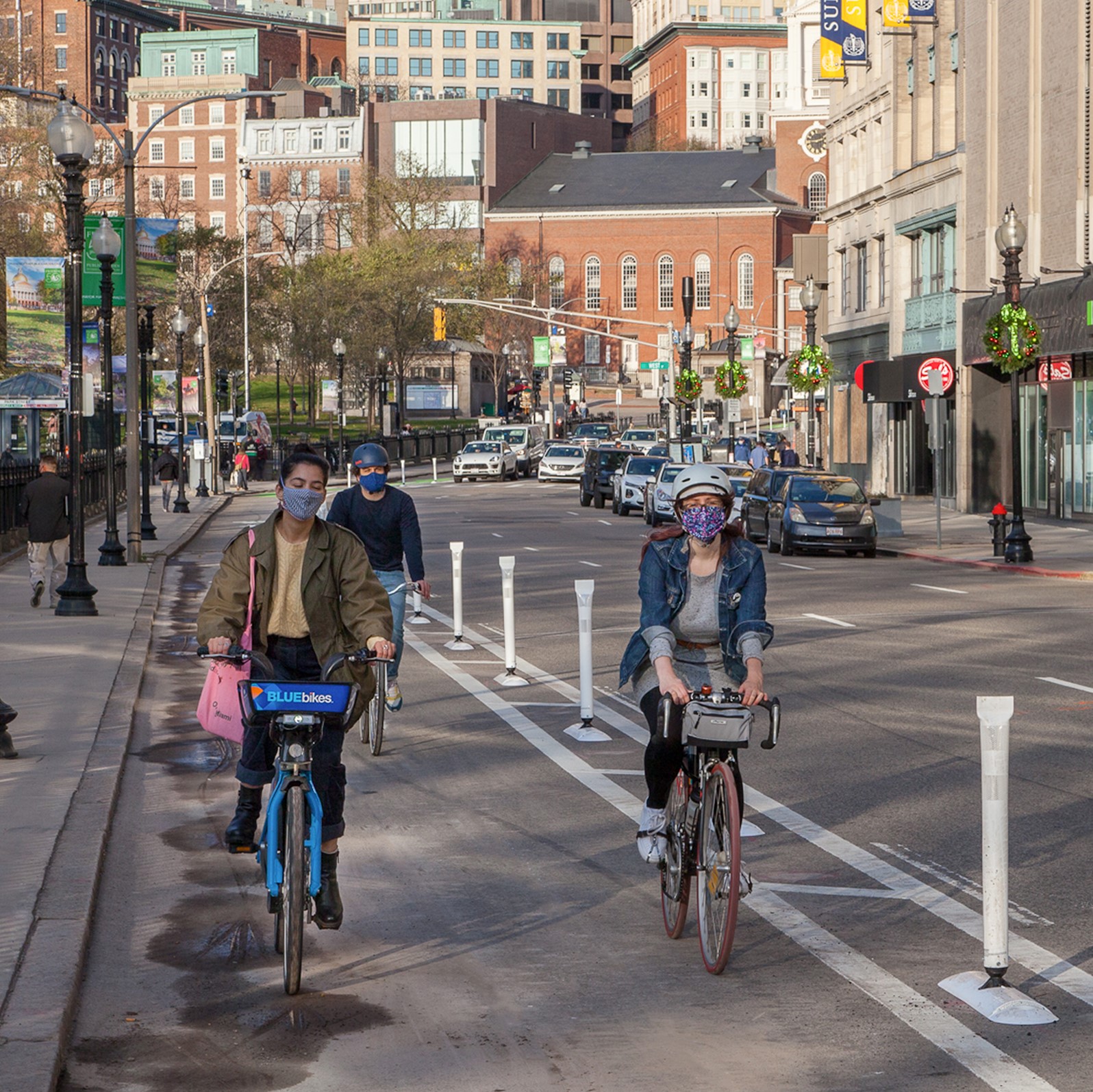 Three bicyclists ride in a protected bike lane with flexposts in the buffer area
