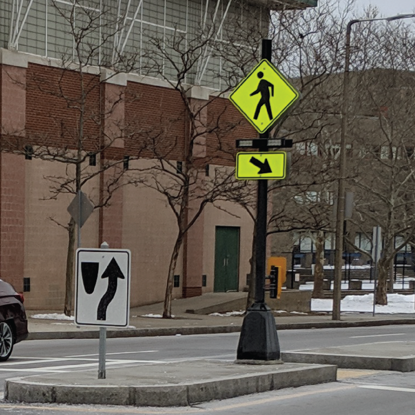 A rapid flashing beacon is installed on a concrete pedestrian crossing island. The beacon is not lit, but you can see the bright yellow sign with a black pedestrian icon and the two rectangular lights.