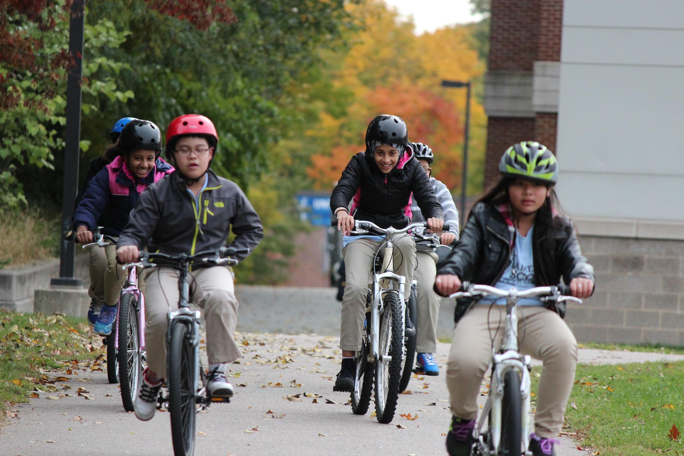 A group of six youth are riding bikes on a path by their school.