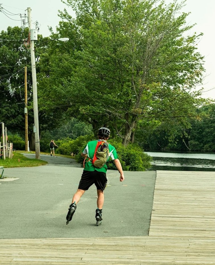 Rollerblader rides in front of view away from camera near stream
