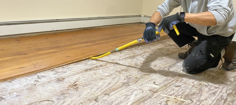 A worker prying up floor boards for reuse