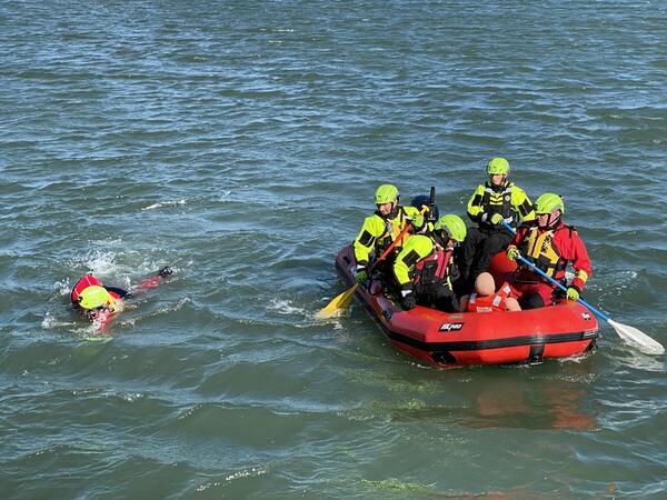 firefighters in a raft, one is in the water swimming