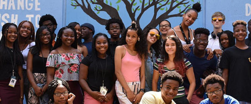 Image shows a group of smiling teens posing for a group picture. 
