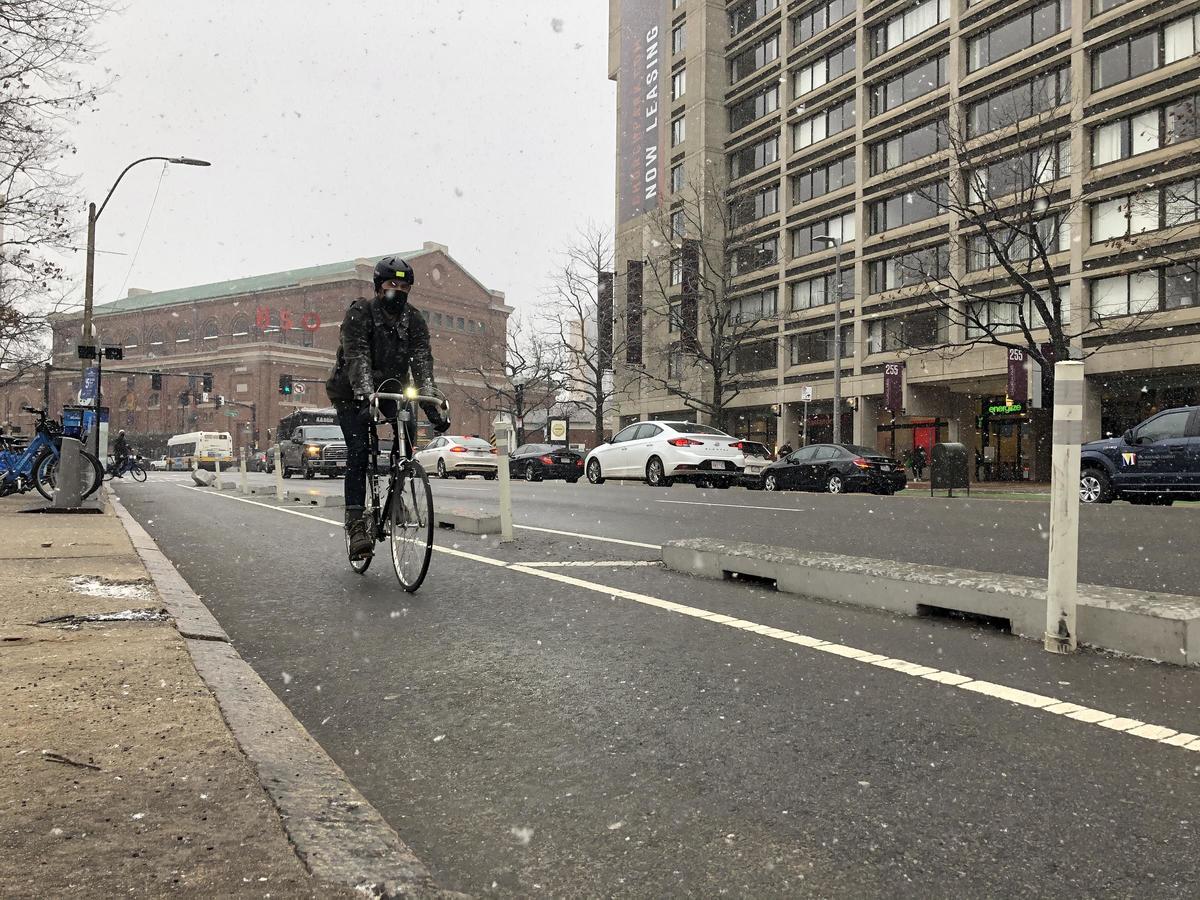 man cycling while it snows on a protected bike lane