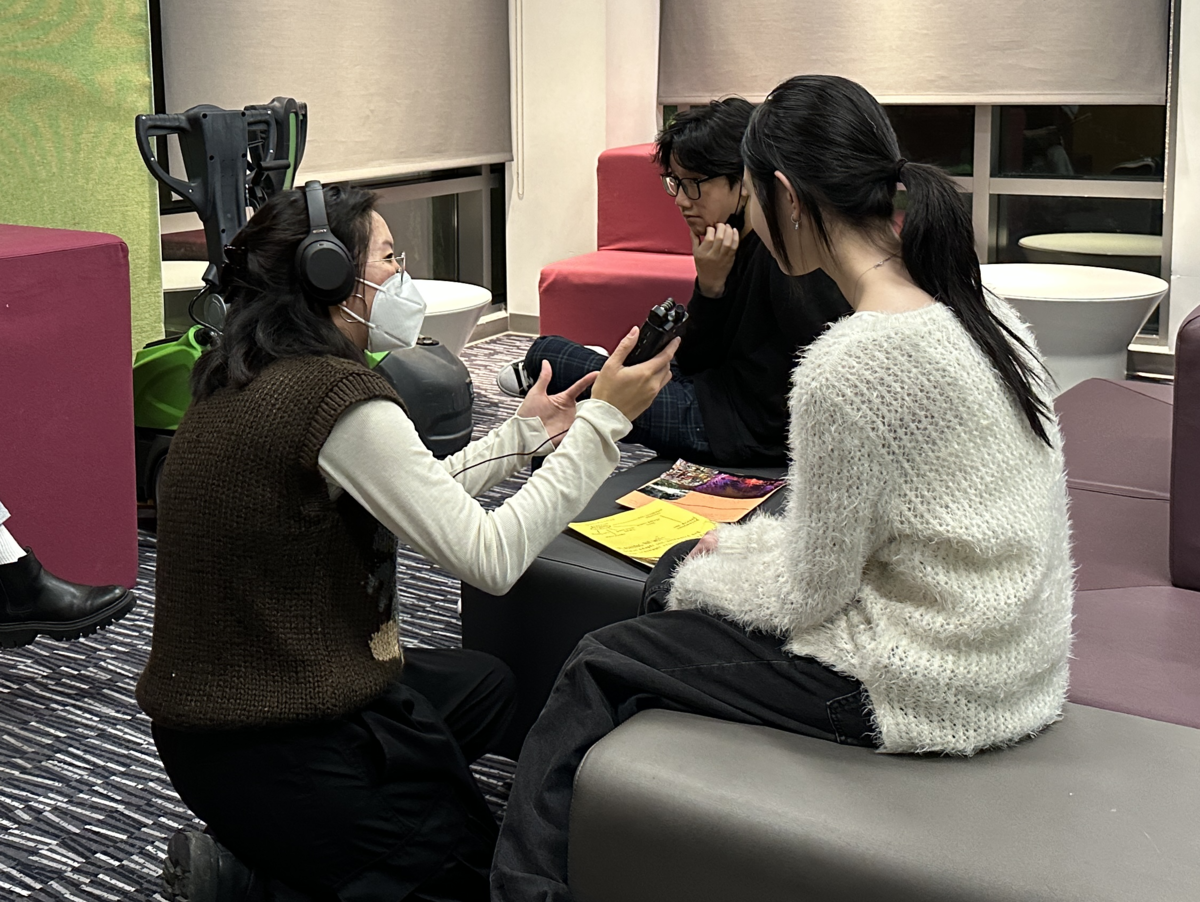 Boston Artist-in-Residence Lily Xie kneels in front of two young people as she uses a microphone to record an interview with them.