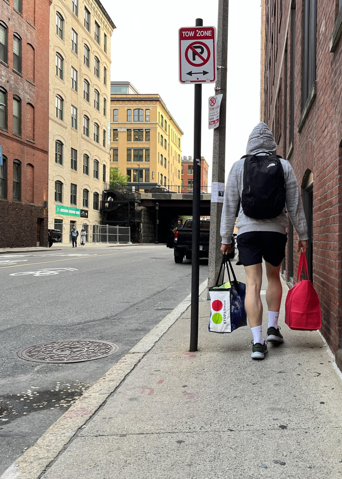A person carrying two bags of groceries squeezes past a sign pole on A Street in the Fort Point neighborhood.
