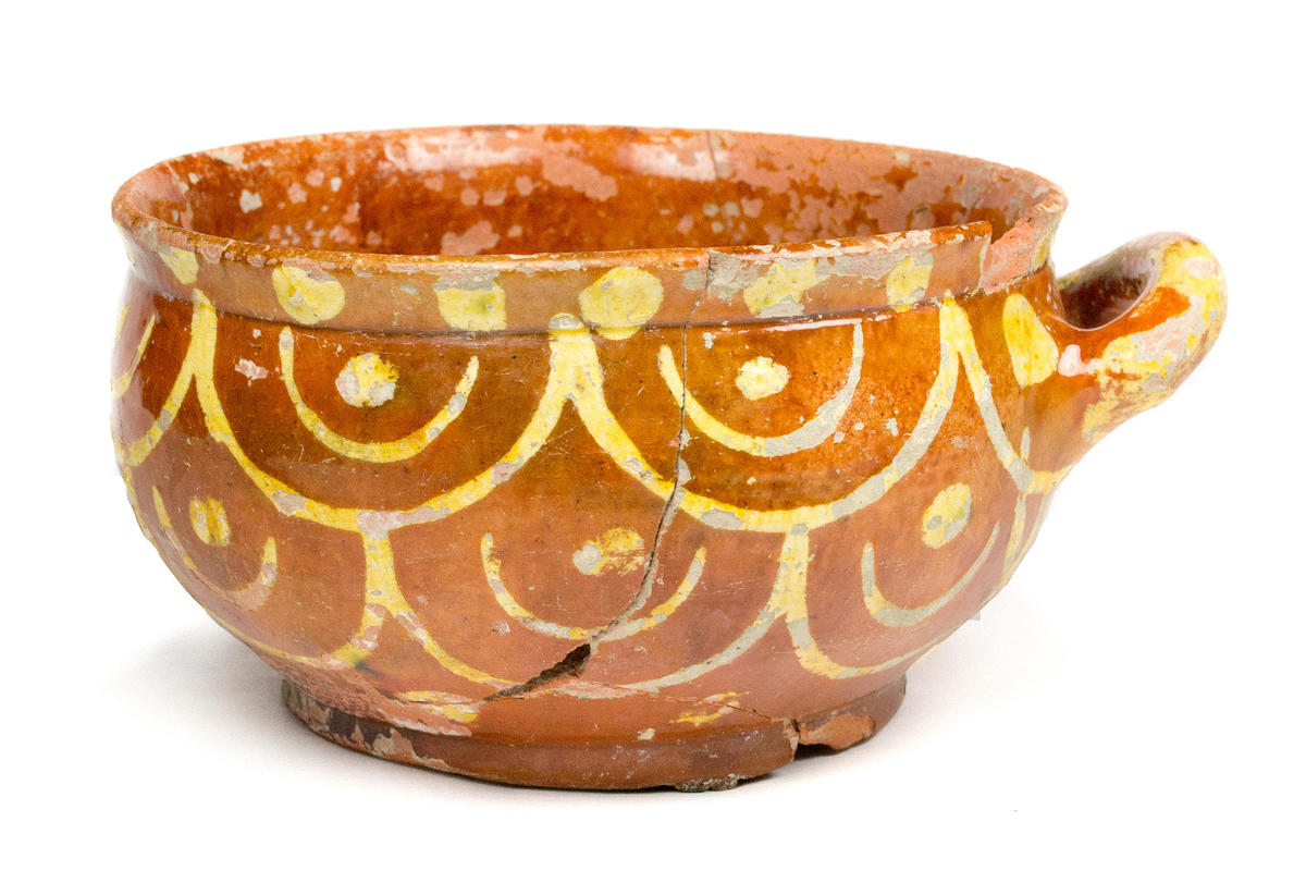 A reconstructed redware porringer decorated with swags and dots in yellow slip.