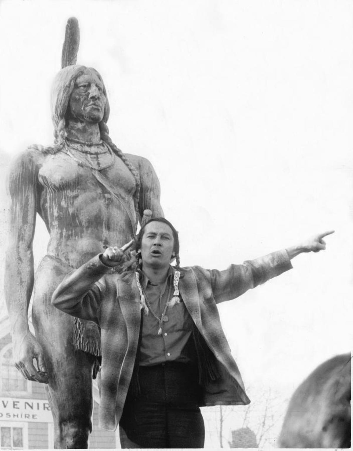A black and white photograph of activist Russell Means giving a speech in front of the Massasoit statue in Plymouth, MA.