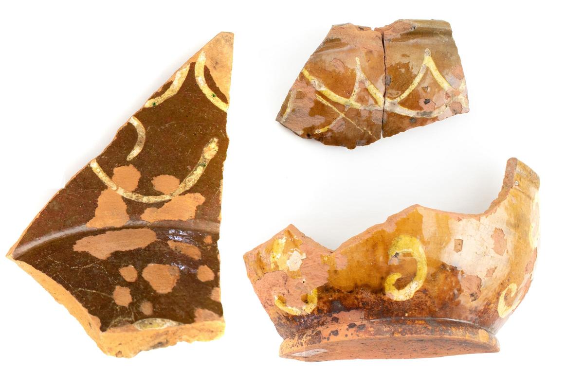 3 fragments of redware pottery vessels decorated with a brown background glaze and swag motifs in yellow slip.