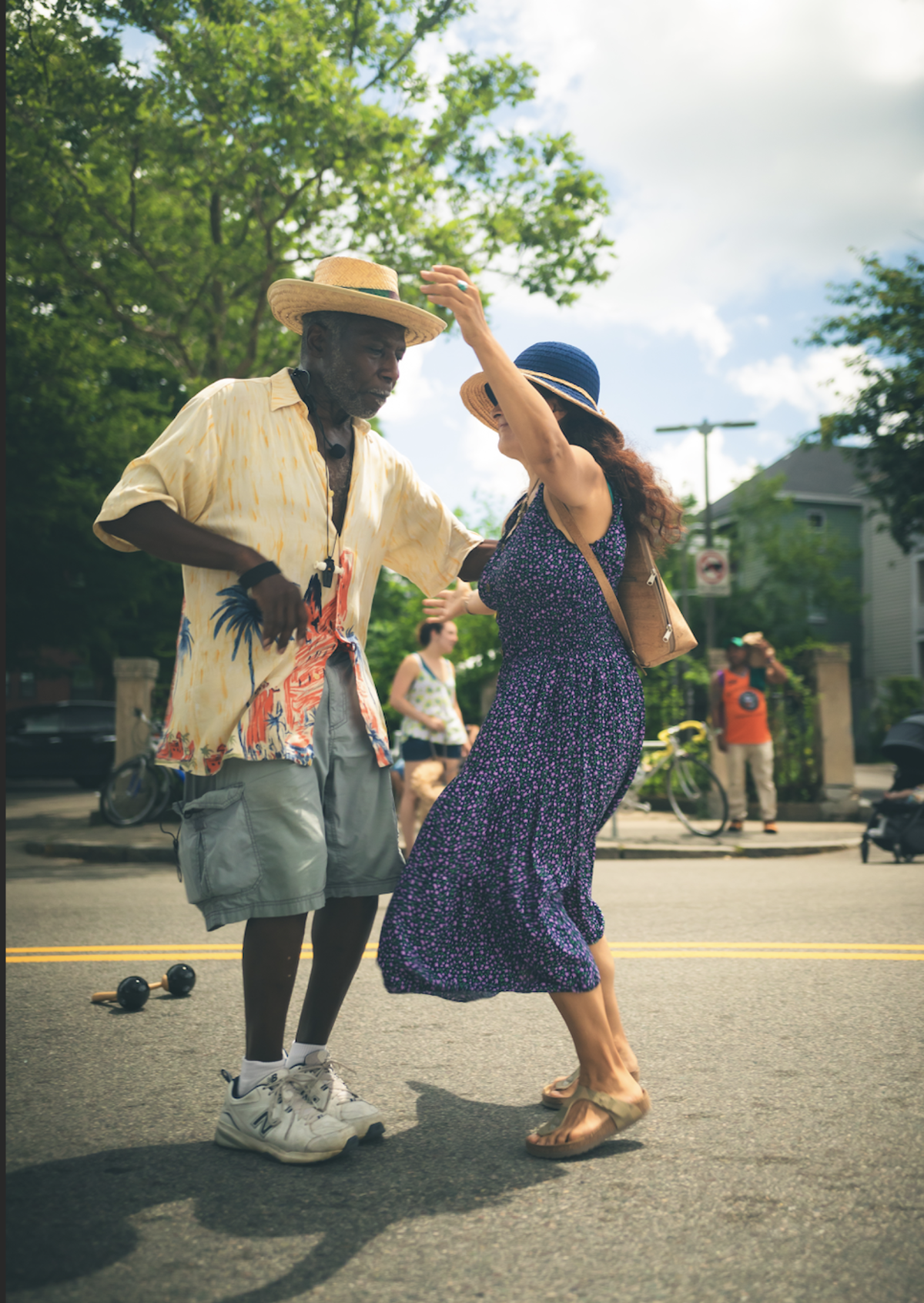 A man in a hat and a woman in a blue dress dance in the middle of the street