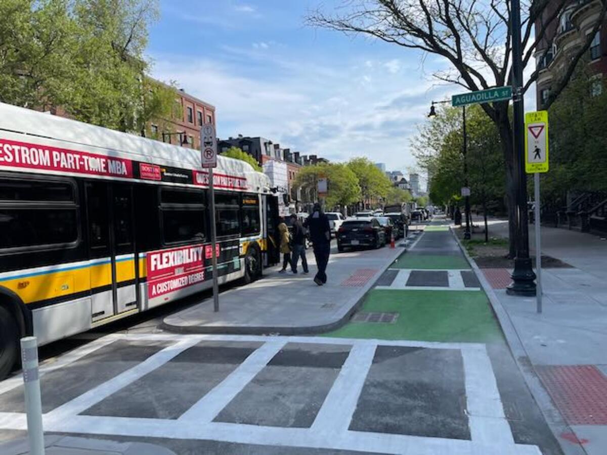 People boarding a bus on Tremont Street. A bike lane runs between the sidewalk and the bus stop