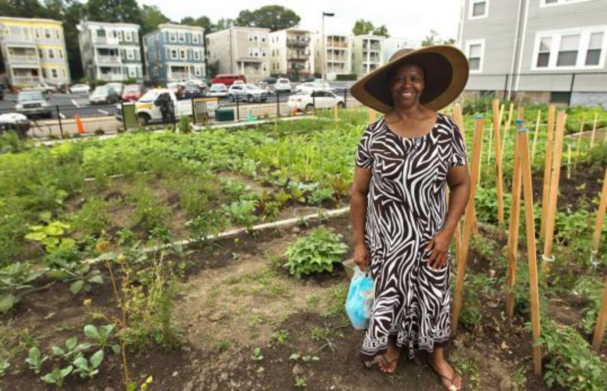 a woman in a zebra print dress and a hat smiling in front of a garden