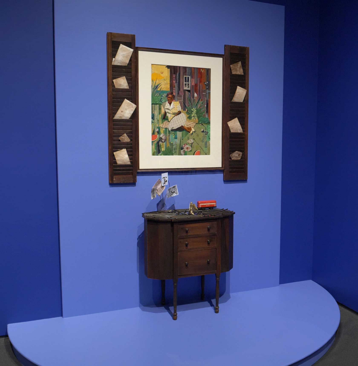A painting of a portrait of a woman laying down. The painting is in a blue room with a table standing in front of it
