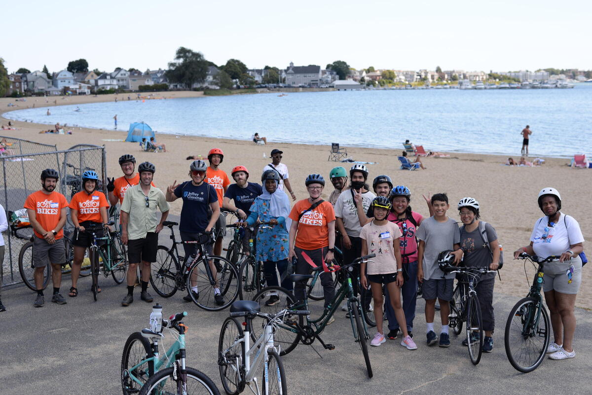 Large group of smiling people posing with bicycles with a beach in the background