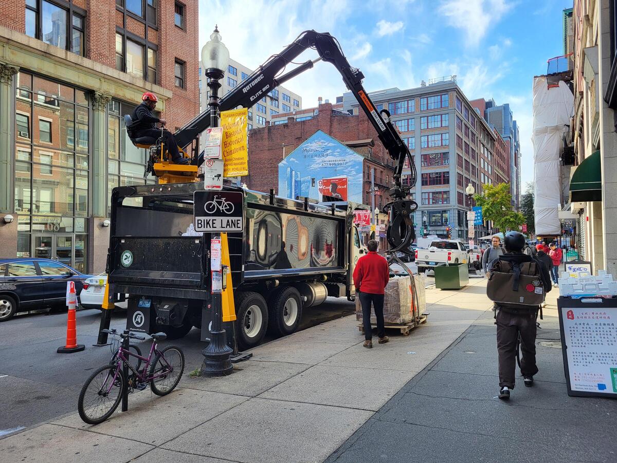 A log truck lowers a planter to the sidewalk, with Urban Forestry Staff at the ready.