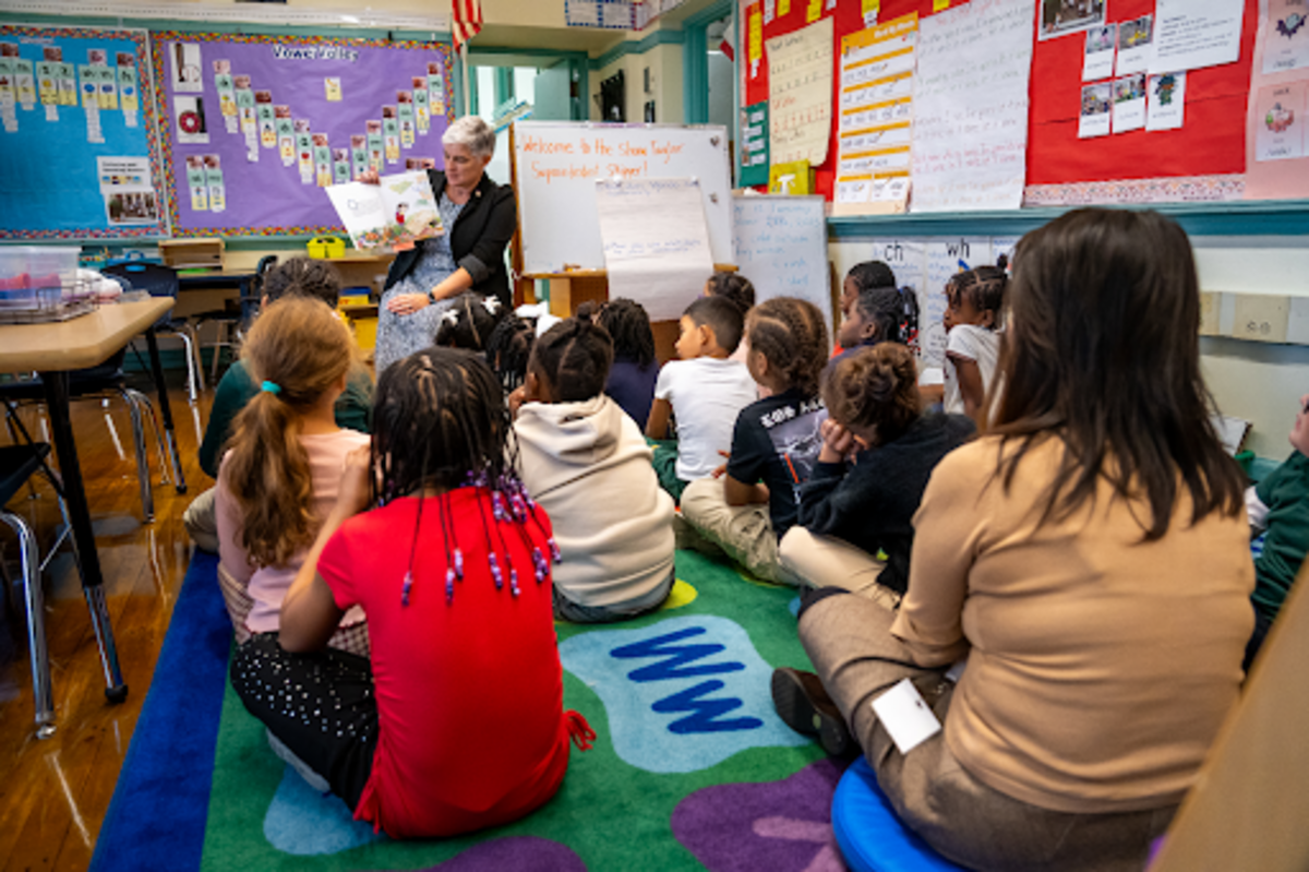 children sit on a rug in front of Kristin McSwain reading a book