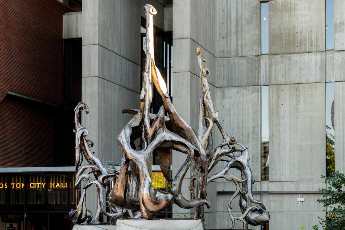 A sculpture made of metal, resembling three birds' wings, stands outside of Boston City Hall.