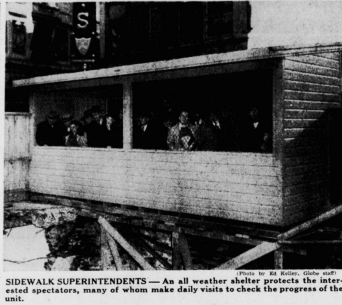 Spectators stand inside a makeshift shelter overseeing a construction site.