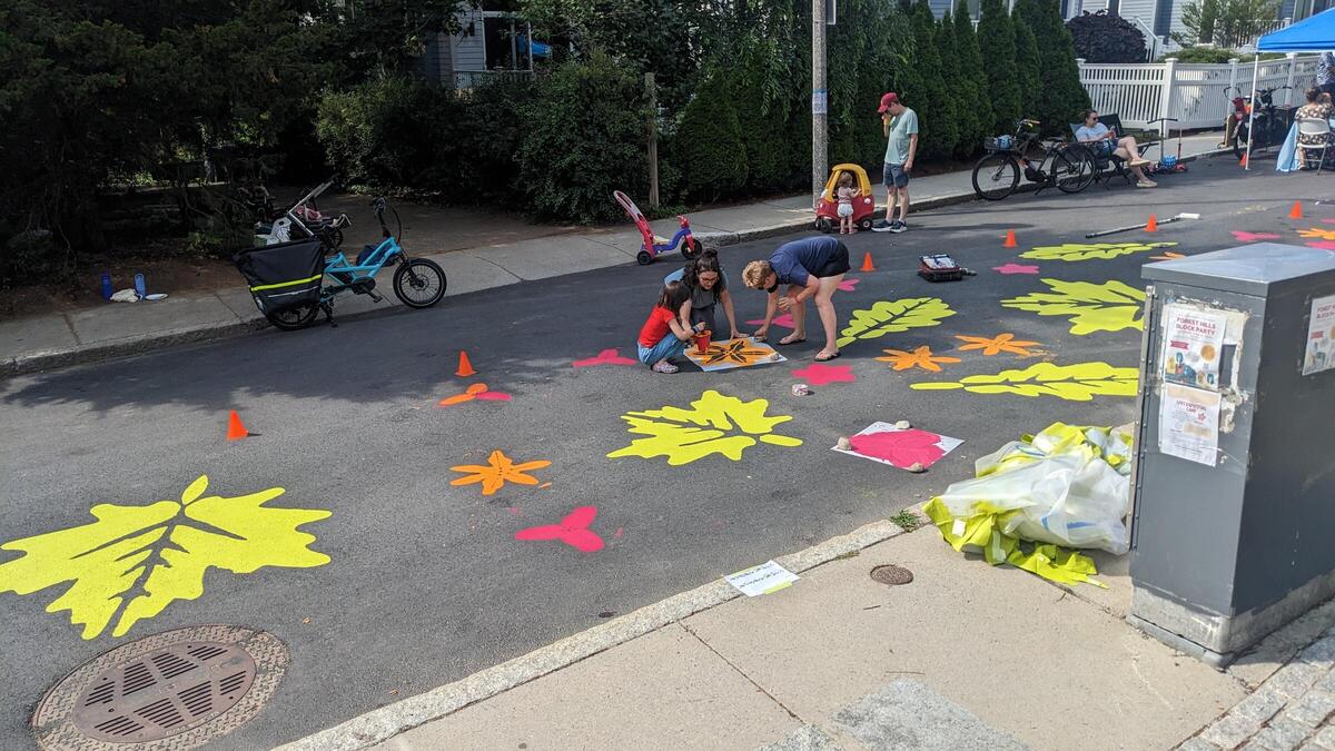 A photo of several people painting large colorful leaves on the street