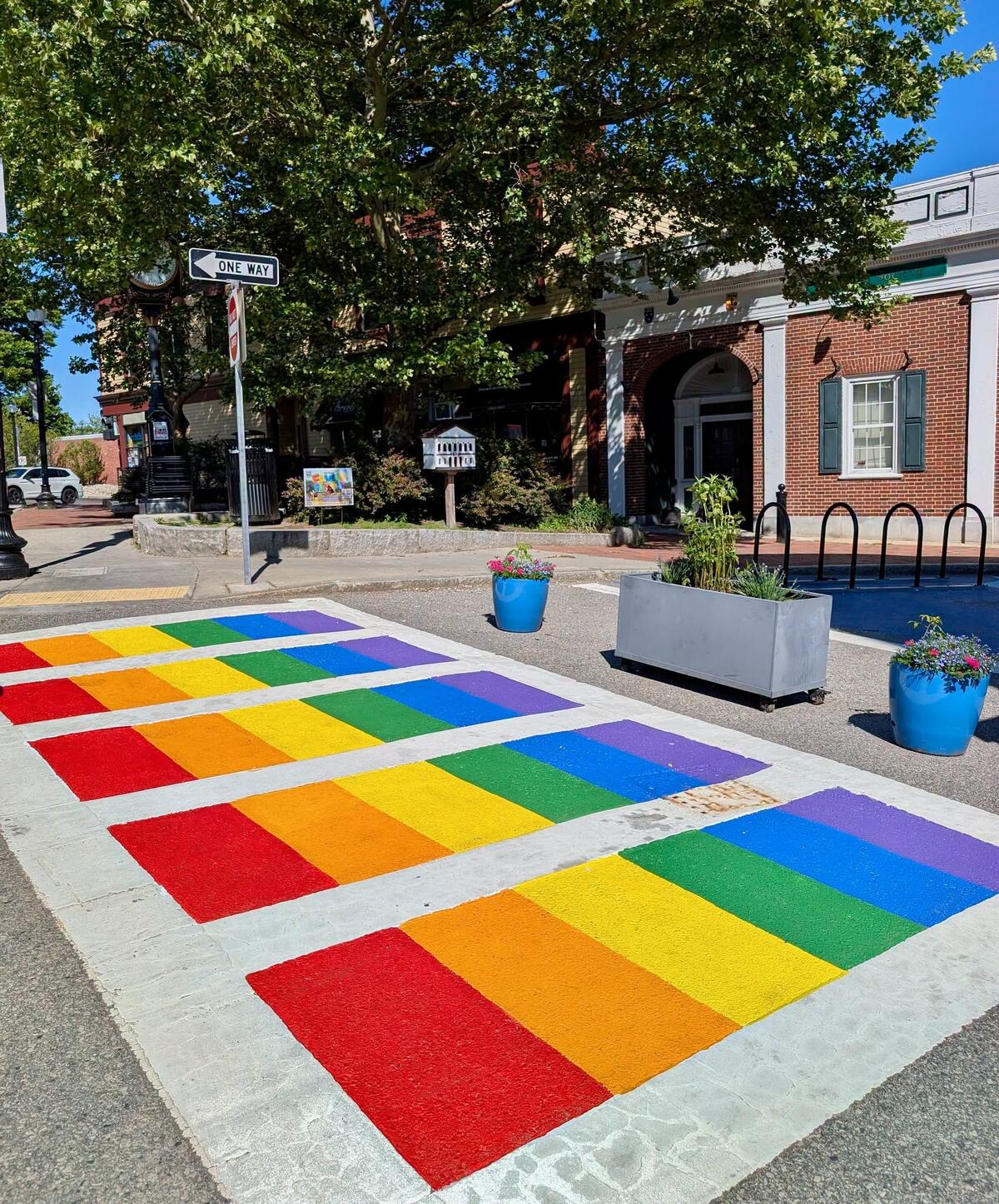 a photo of a crosswalk that has been painted with rainbow colors between the white crosswalk markings