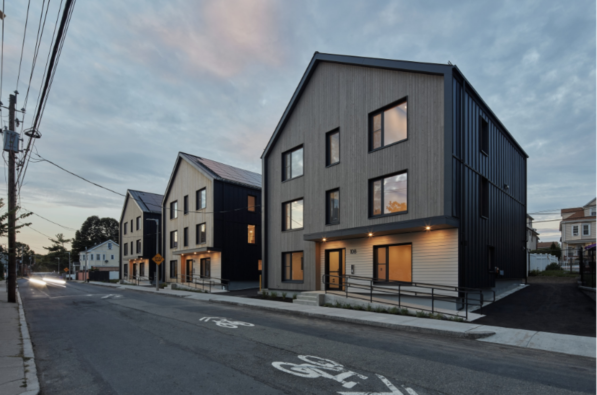 3 modern gray homes with orange-lit windows on a sunset sky. 