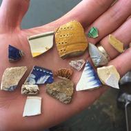 A close up of a hand holding an assortment of ceramic sherds ranging from the 17th to 19th centuries in date.