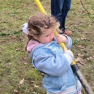 A young child holds a shovel that is far too big for her.