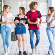 Group of young adults, possibly students, walking and talking together outdoors, some wearing backpacks.