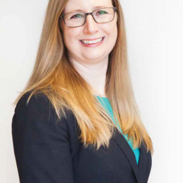 A photo from the waist-up of board member Teresa Anderson, wearing a blazer with a white background